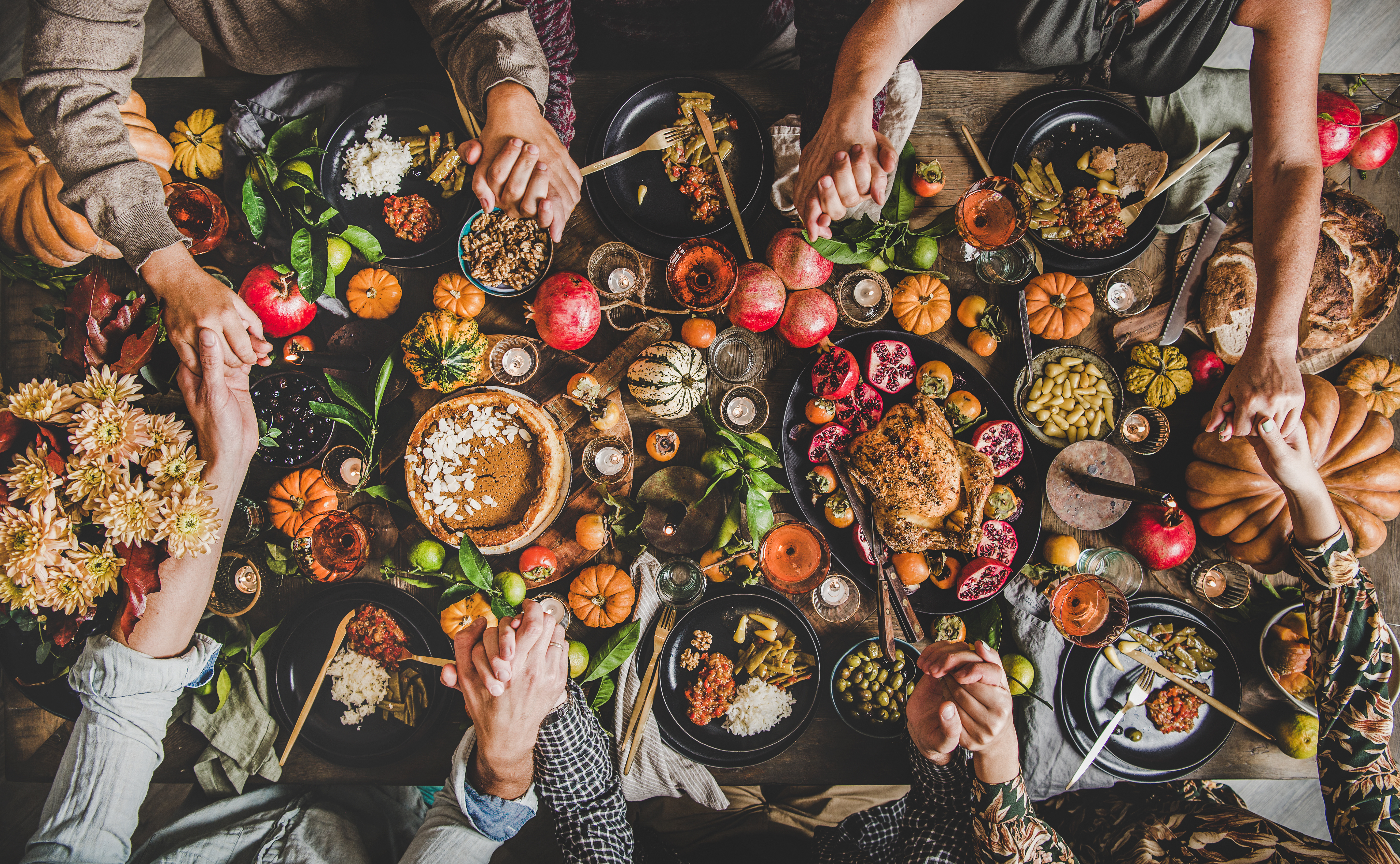 Photo of friends and family holding hands around a table of Thanksgiving food